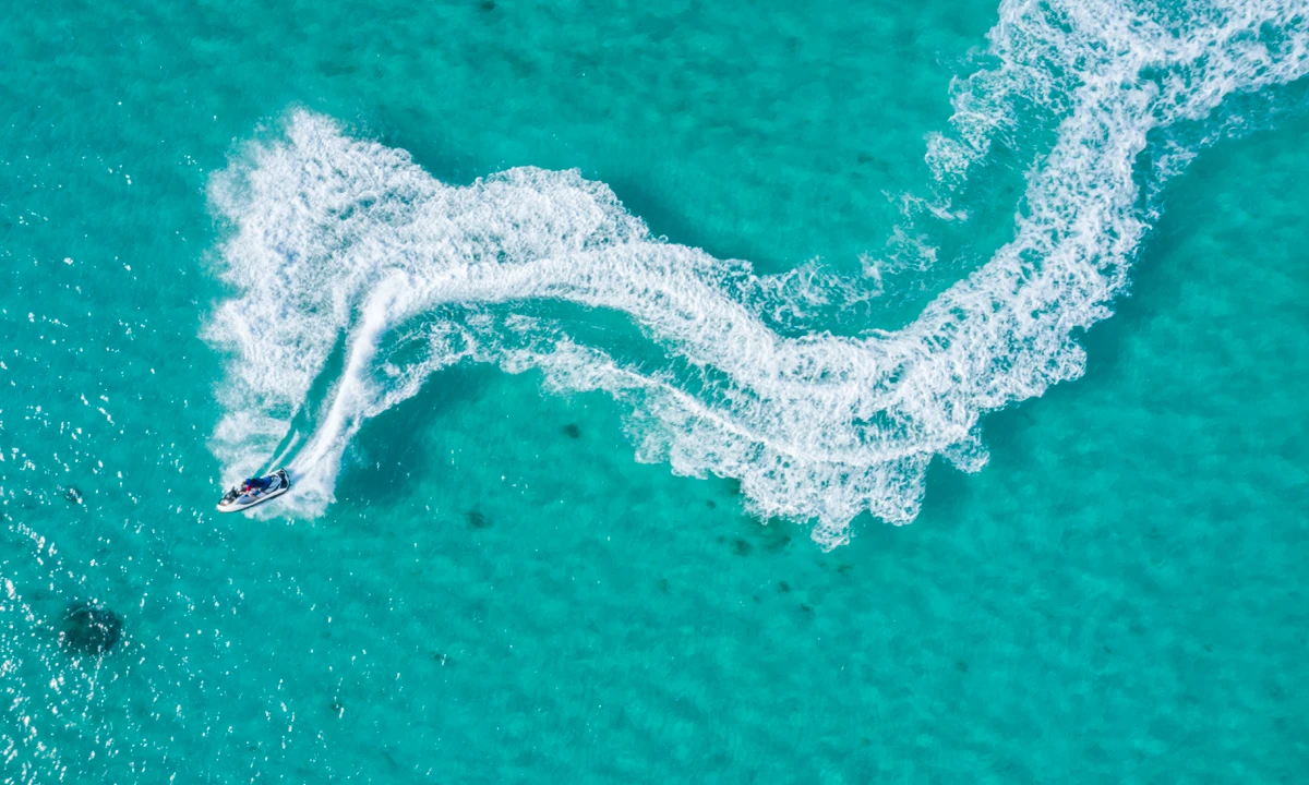 Ba&ntilde;ista en moto acu&aacute;tica sobre ola blanca en mar turquesa