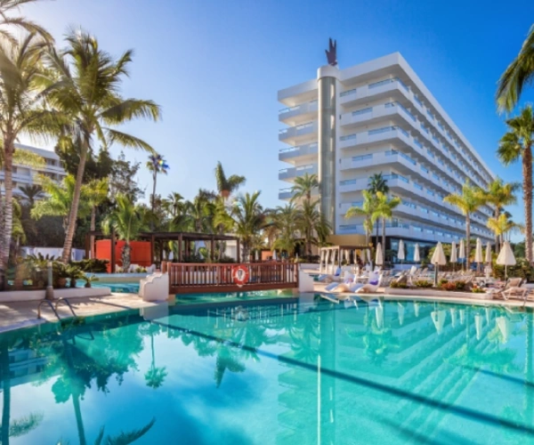 Piscina azul con palmeras y hotel blanco de varios pisos al fondo