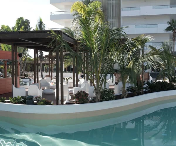 Piscina y zona de descanso con palmeras frente a un hotel moderno