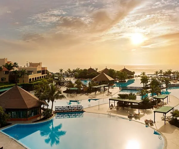 Vista de resort con varias piscinas y palmeras al atardecer