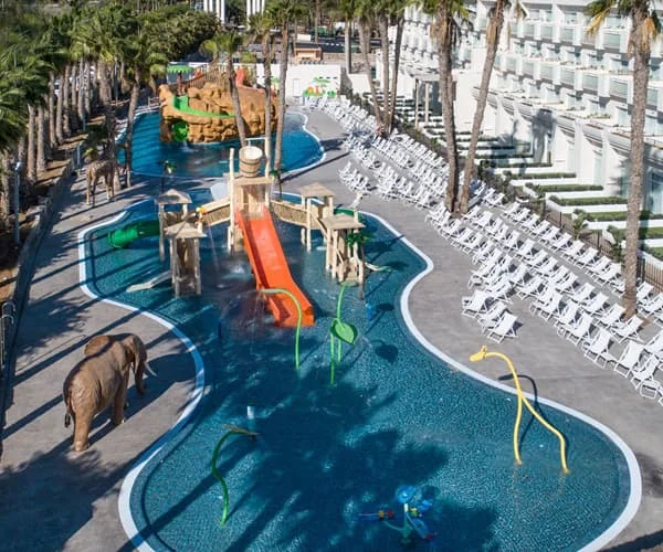 Piscinas y hamacas en resort con palmeras y figuras de elefantes