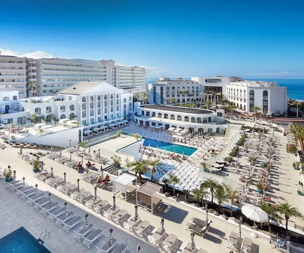 Hotel junto al mar con piscina, tumbonas y palmeras en la costa
