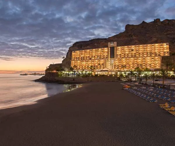 Hotel iluminado al atardecer junto al mar y una playa oscura
