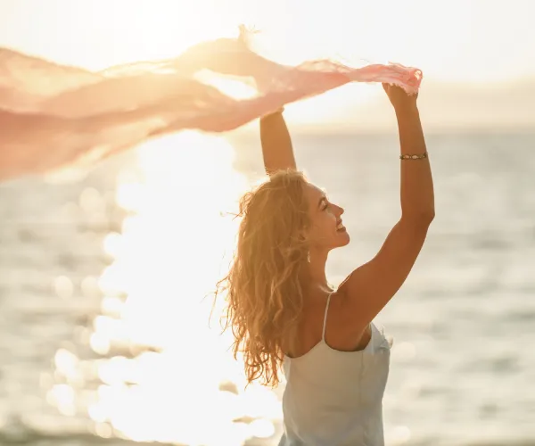 Mujer en la playa alza los brazos bajo el atardecer