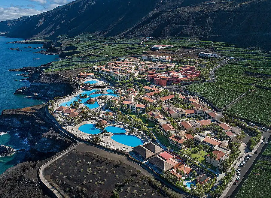 Vista a&eacute;rea de un complejo tur&iacute;stico con piscinas junto al mar y monta&ntilde;as.
