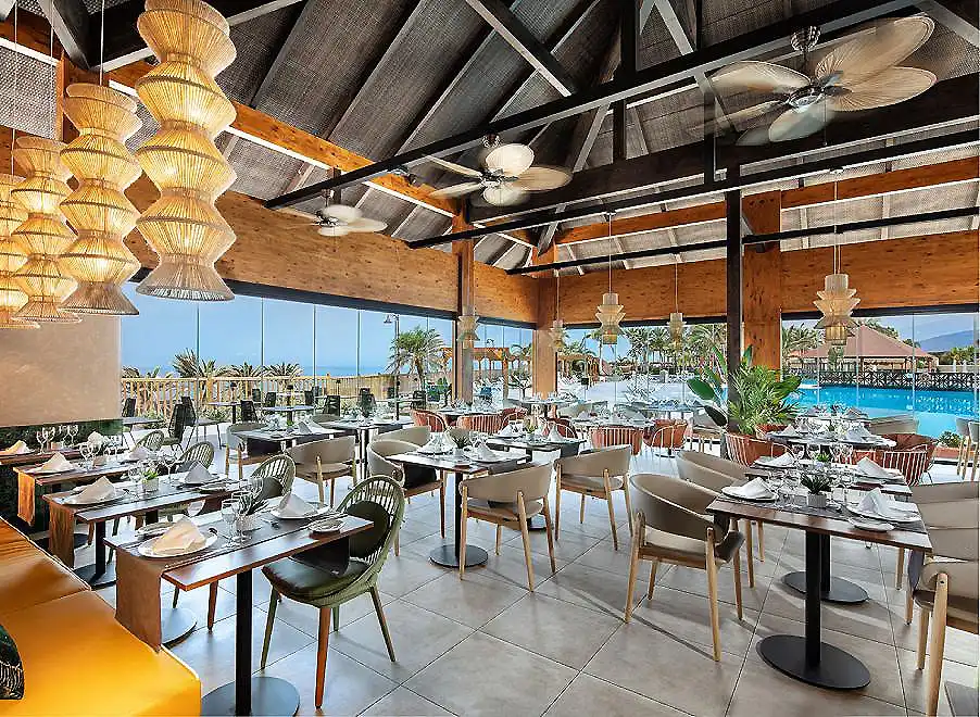 Comedor con mesas servidas, l&aacute;mparas de mimbre y vistas a piscina.