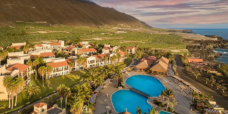 Vista a&eacute;rea de un hotel con piscina azul y palmeras junto al mar