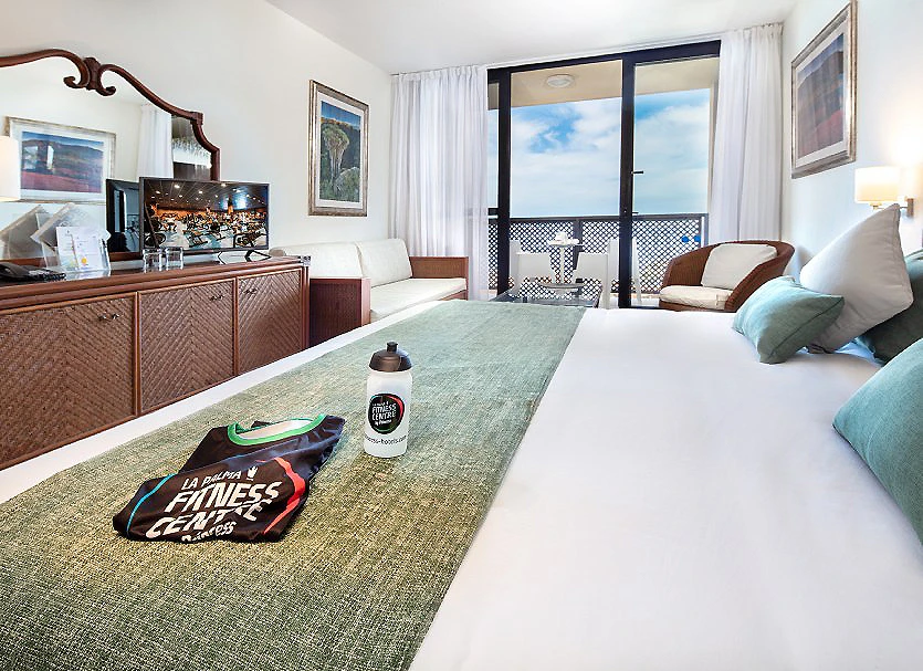Habitaci&oacute;n hotelera con cama doble, sof&aacute; y balc&oacute;n con vistas al mar.
