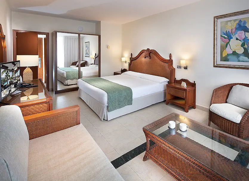 Habitaci&oacute;n de hotel con cama doble, sillones y decoraci&oacute;n moderna.