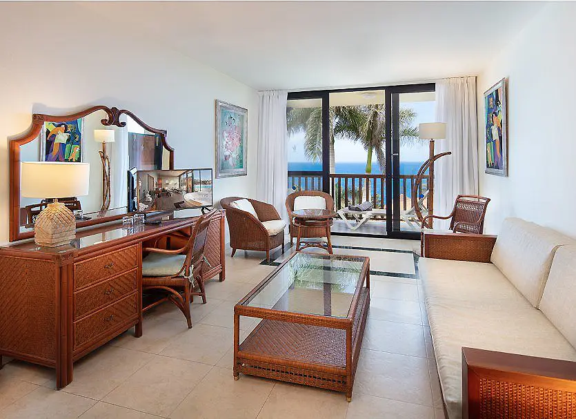 Sala de estar luminosa con muebles de madera, sof&aacute; y vista al mar.