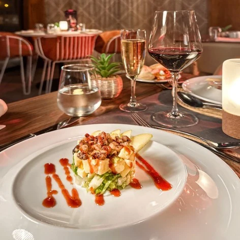 Plato con ensalada y salsa, copas de vino y mesa decorada en restaurante.