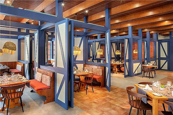 Comedor r&uacute;stico con mesas, sillas y vigas azules en un espacio interior.
