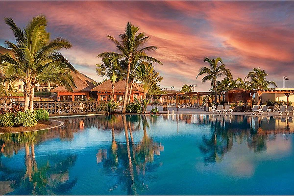 Piscina tropical al atardecer con palmeras reflejadas en el agua