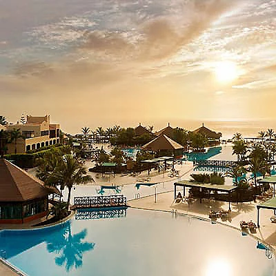Atardecer sobre hotel con piscinas y palmeras junto al mar