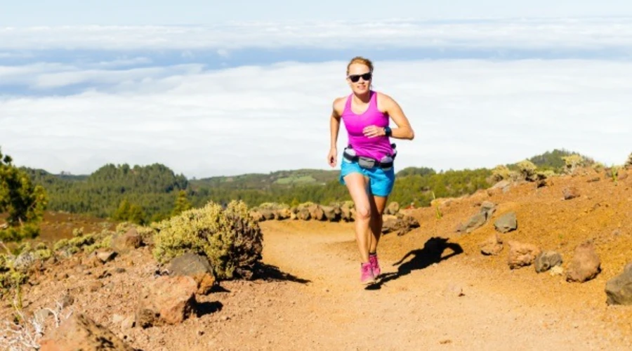 Mujer corriendo con ropa deportiva en un sendero de monta&ntilde;a bajo el sol