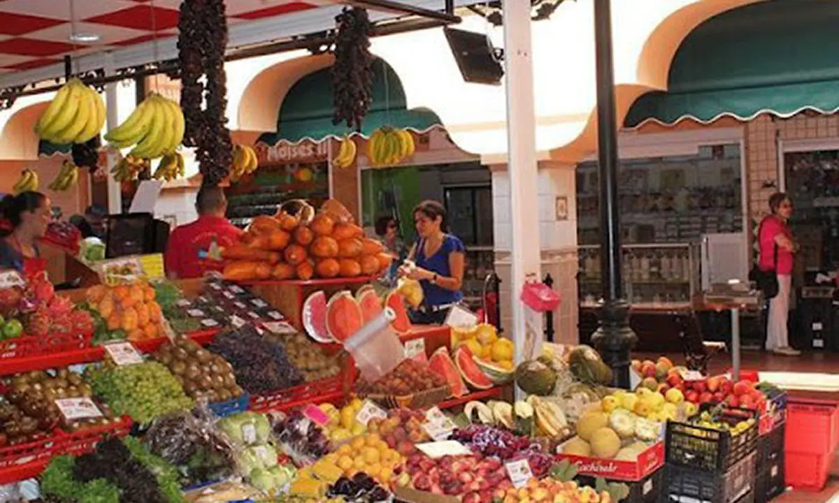 Puesto de frutas y verduras en mercado al aire libre con bananos y uvas
