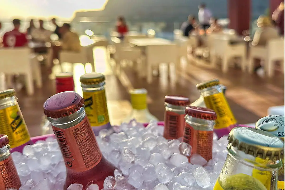 Botellas sobre cubitos de hielo; fondo con gente desenfocada en un evento