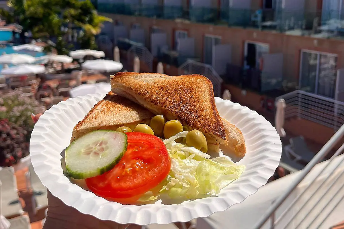 S&aacute;ndwich tostado con pepino, tomate, lechuga y aceitunas en una bandeja blanca