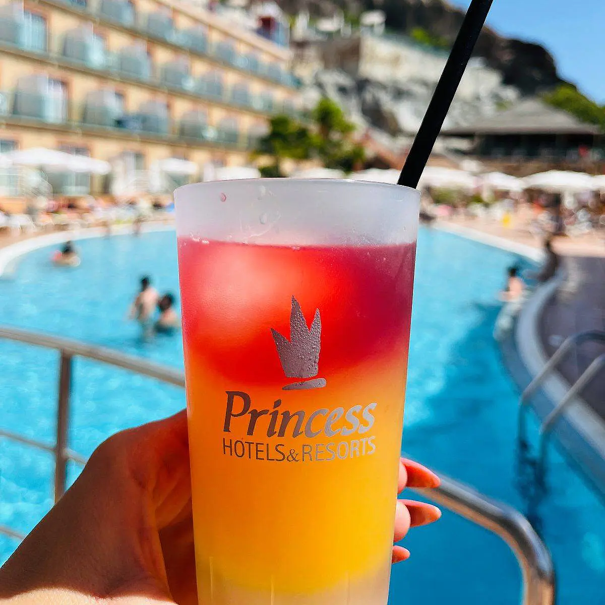 Vaso de bebida Princess Hotels con pajilla junto a una piscina azul
