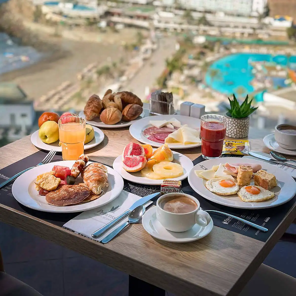 Desayuno con platos de frutas, huevos y jugos frente a una piscina.