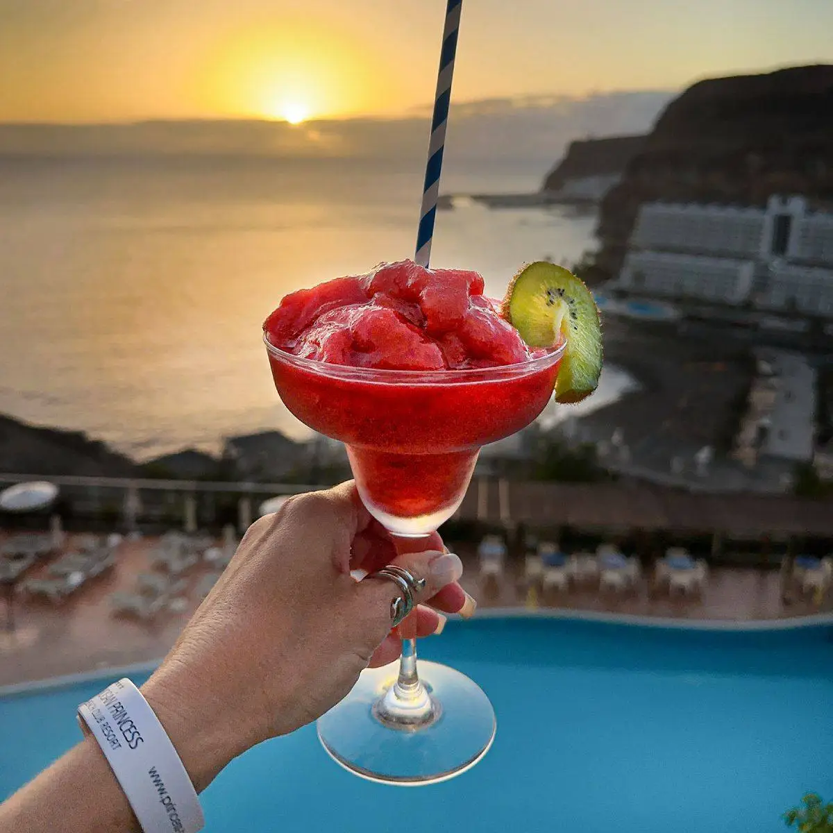 C&oacute;ctel rojo con frutas y pajilla, a la puesta de sol junto a piscina