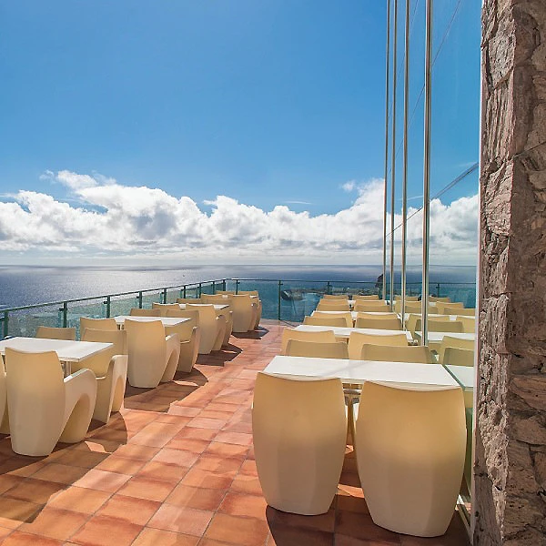 Terraza con mesas y sillas frente al mar y cielo azul con nubes.