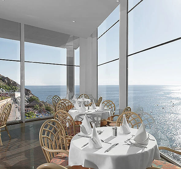 Mesa servida en terraza con vista al mar y monta&ntilde;as, ventanales de vidrio