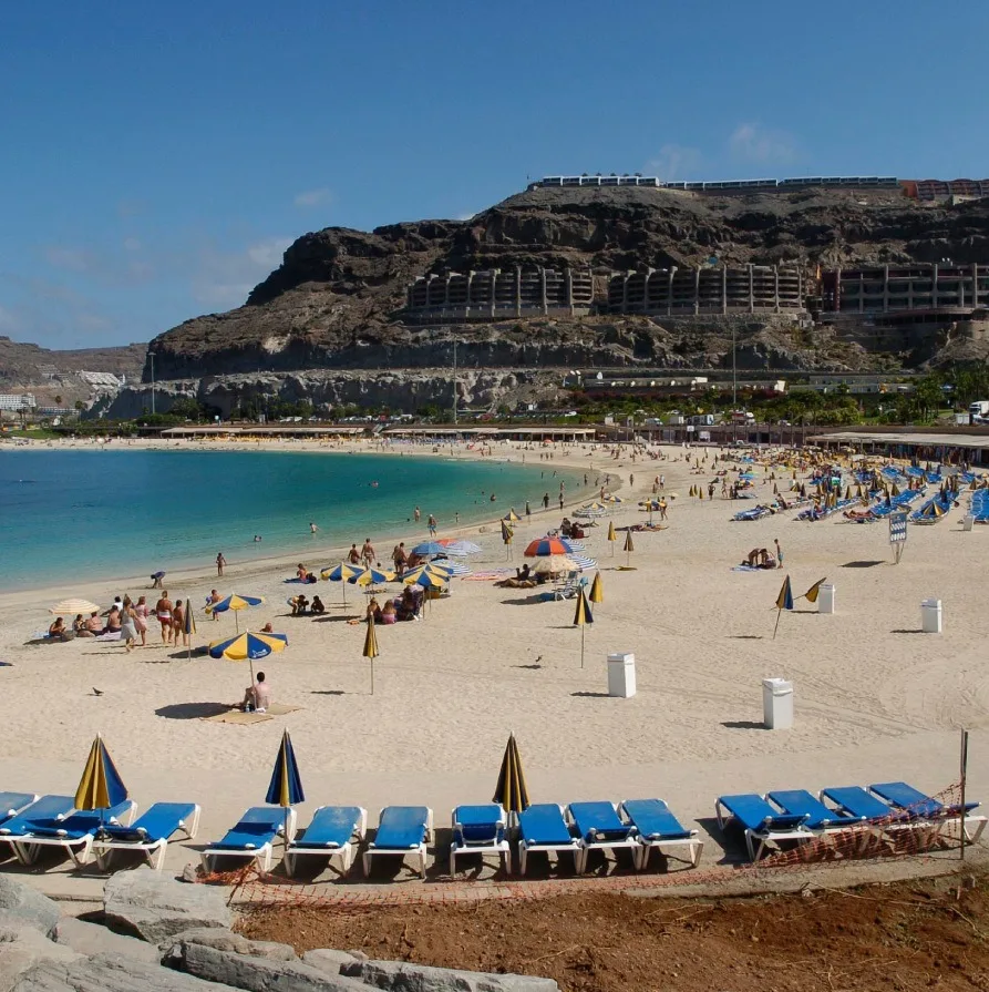 Playa con sombrillas y hamacas junto a un acantilado y un hotel costero