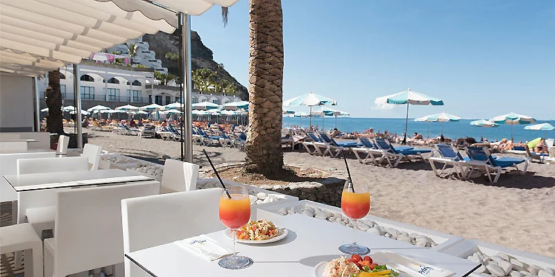 Terraza con mesa y bebidas, sillas y sombrillas junto a la playa