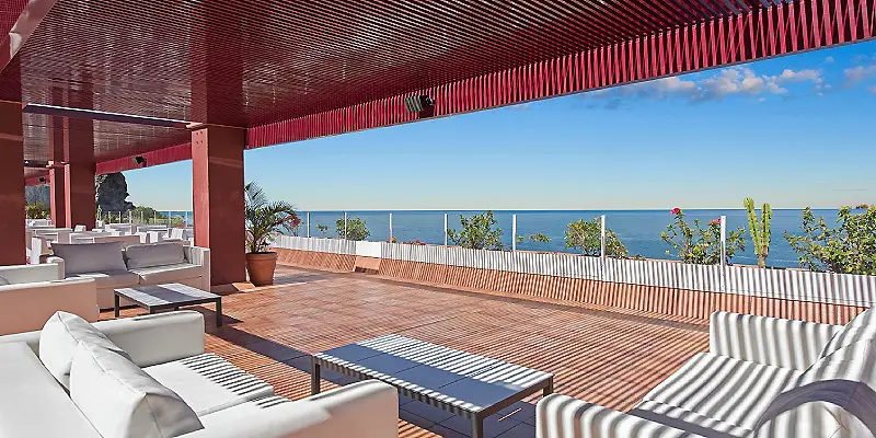 Terraza moderna con muebles y vista al mar bajo techo rojo.