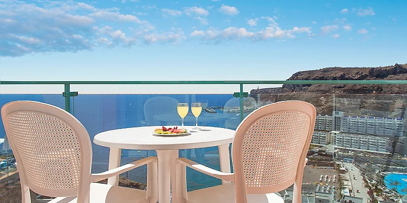 Mesa con dos copas y vistas al mar desde un balc&oacute;n con cielo azul.