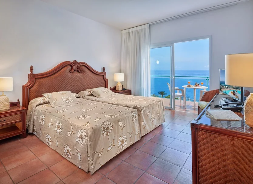 Dormitorio con cama de madera y vista al mar desde el balc&oacute;n, habitaci&oacute;n.