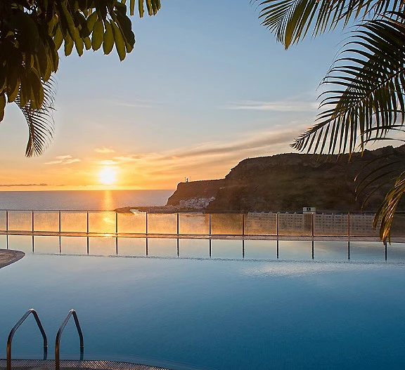 Atardecer en piscina con palmeras y acantilado al fondo