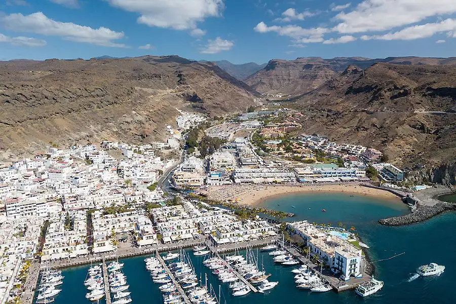 Vista a&eacute;rea de un puerto con yates y una bah&iacute;a junto a un pueblo costero.