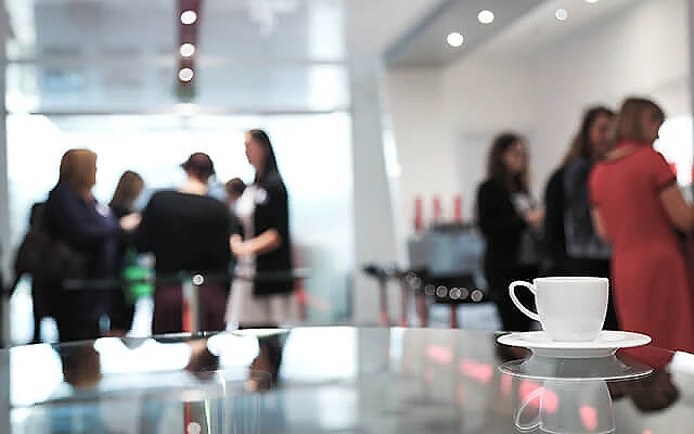Caf&eacute; en primer plano y personas conversando en un evento corporativo.
