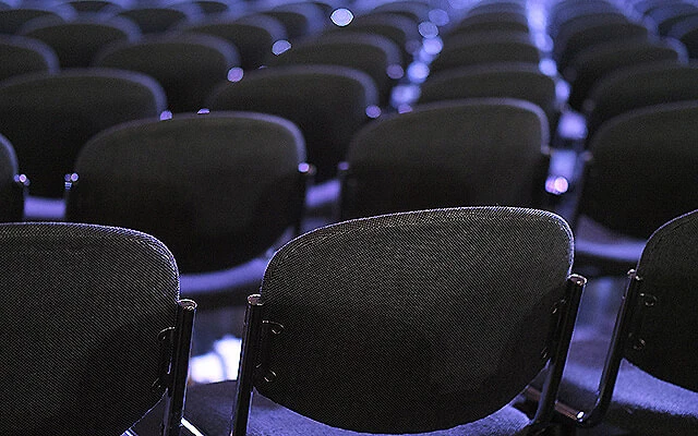 Filas de sillas vac&iacute;as en un auditorio con luces azules difusas