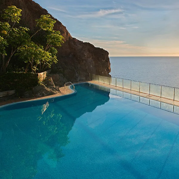 Piscina con vista al oc&eacute;ano y acantilado, atardecer, naturaleza tropical.
