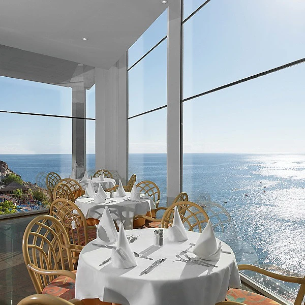 Mesa con mantel blanco y sillas de mimbre, frente al mar desde un balc&oacute;n