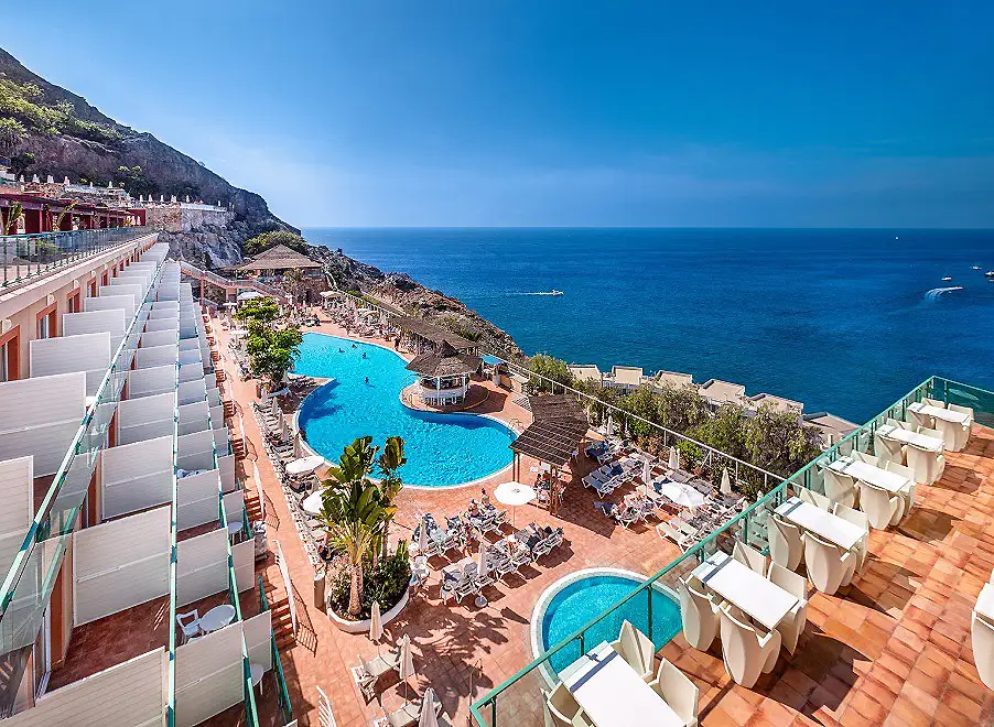 Balcones y piscina en un hotel frente al mar, con acantilado y tumbonas