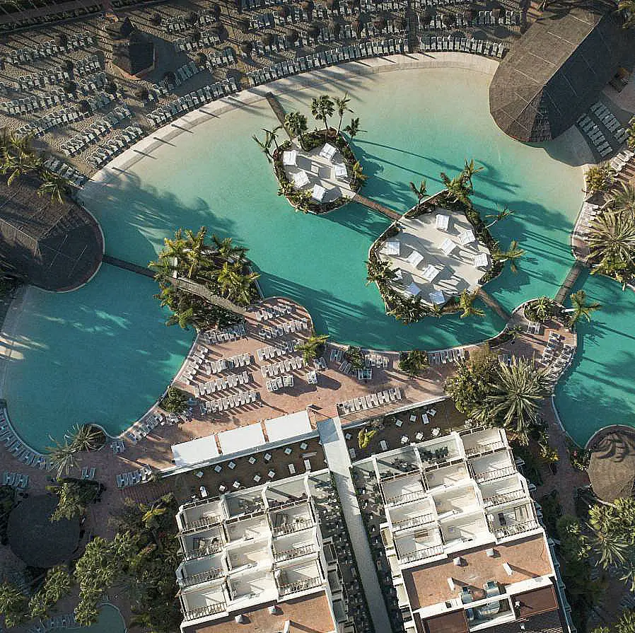 Vista a&eacute;rea de una piscina azul en un complejo residencial con jardines y edificios
