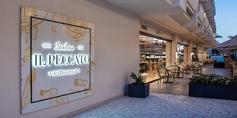 Cartel luminoso de Il Peccato restaurante junto a terraza con mesas.