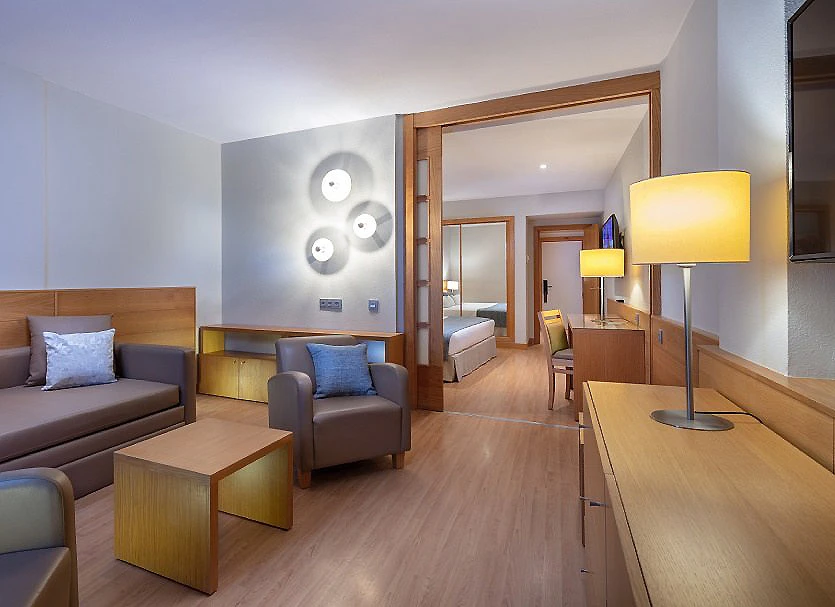 Sala de hotel moderna con sillones grises, mesa de madera y l&aacute;mparas.