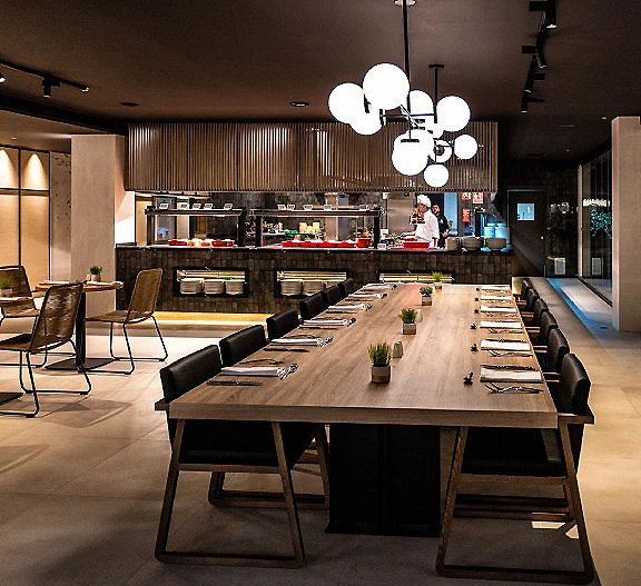 Sala moderna con mesa larga y sillas, bar al fondo e iluminaci&oacute;n colgante