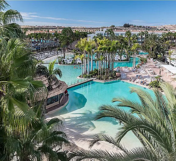 Piscina tropical con palmeras, tumbonas y vista al complejo hotelero.