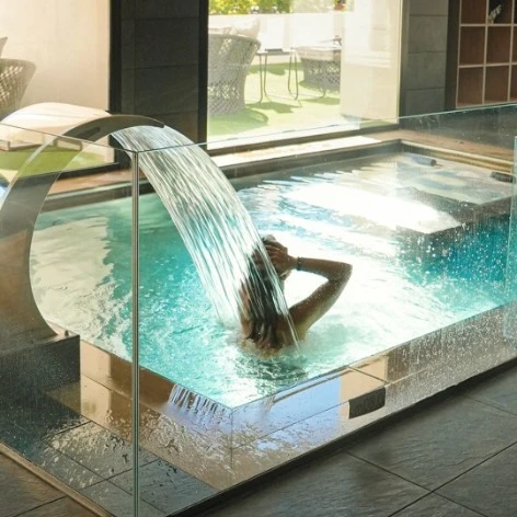 Chorro de agua en una ba&ntilde;era termal interior con jard&iacute;n al fondo