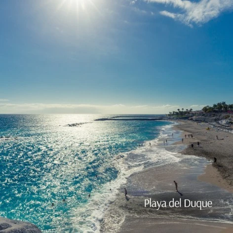 Playa del Duque, mar azul y olas rompiendo con cielo despejado.