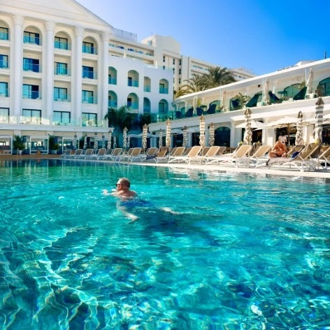 Piscina de hotel con edificio blanco y persona nadando bajo el sol