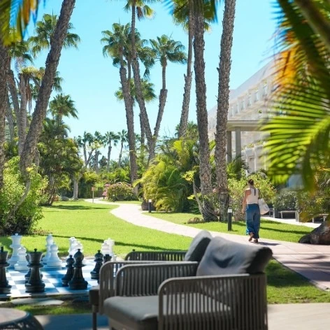 Jard&iacute;n tropical con palmeras y ajedrez gigante al aire libre.