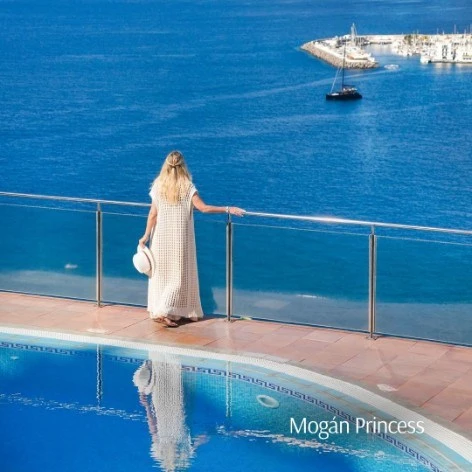 Mujer con vestido blanco mirando el mar, barcos y reflejo en la piscina