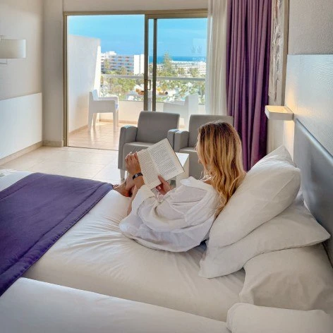 Mujer leyendo en la cama junto a una ventana con cortinas moradas